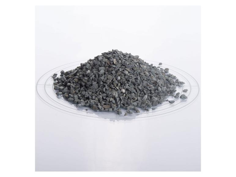 Haufen grauer Kieselsteine auf einer transparenten Platte mit Messmarkierungen.