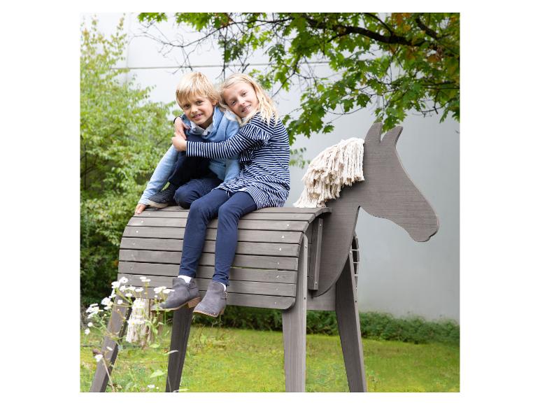 Zwei Kinder spielen auf einem hölzernen Schaukelpferd im Garten.