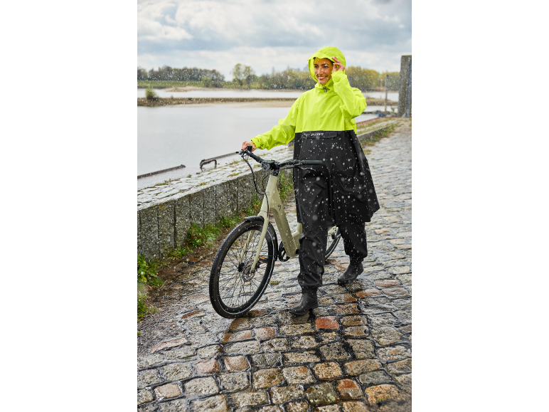 Frau in gelb-schwarzer Regenjacke geht mit ihrem Fahrrad im Regen.