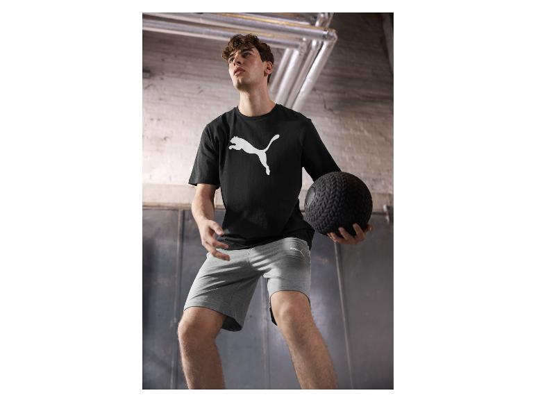 Mann in Puma Shirt und Shorts, hält einen Medizinball.