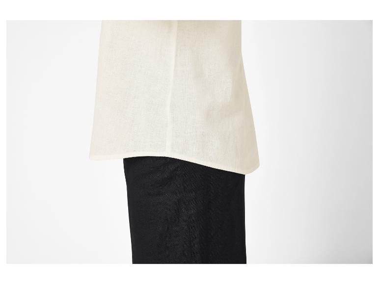 Nahaufnahme einer Person, die ein cremefarbenes Leinentop über einer schwarzen Hose trägt.