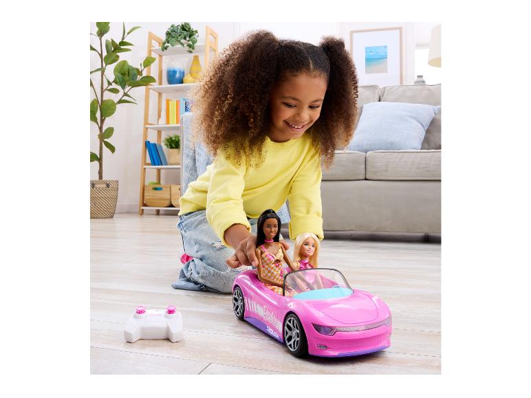 Mädchen spielt mit einem pinken ferngesteuerten Auto mit zwei Puppen im Wohnzimmer.