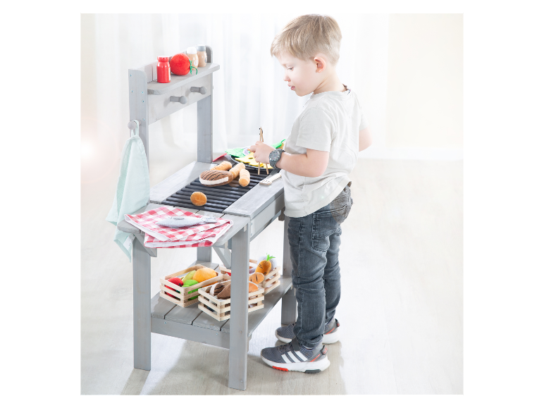 Kind spielt mit einem hölzernen Spielzeuggrill.