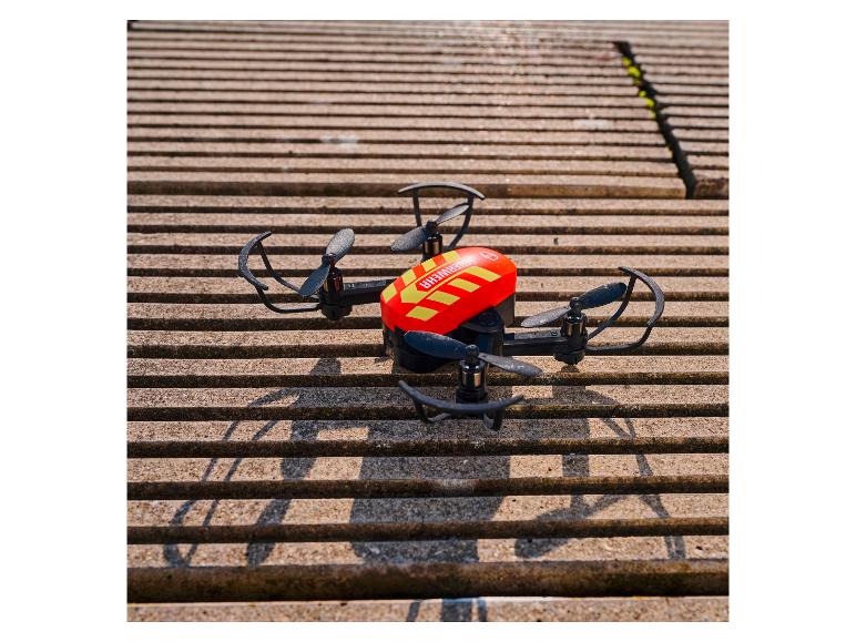 Rote und schwarze Drohne mit Propellern auf einer gestreiften Betonoberfläche.