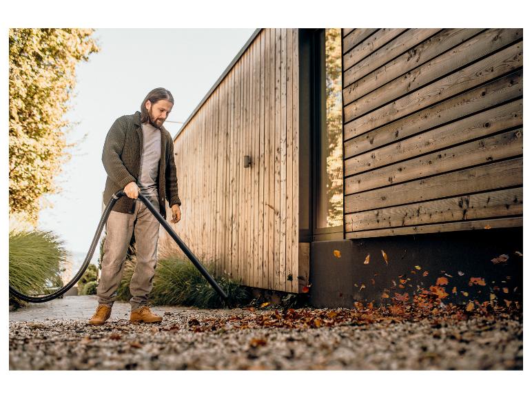 Mann mit Laubbläser entfernt Laub neben einem Holzhaus.