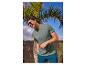 Mann in grünem T-Shirt mit 'Thrive in the unknown' Text, blauen Shorts und Sonnenbrille.