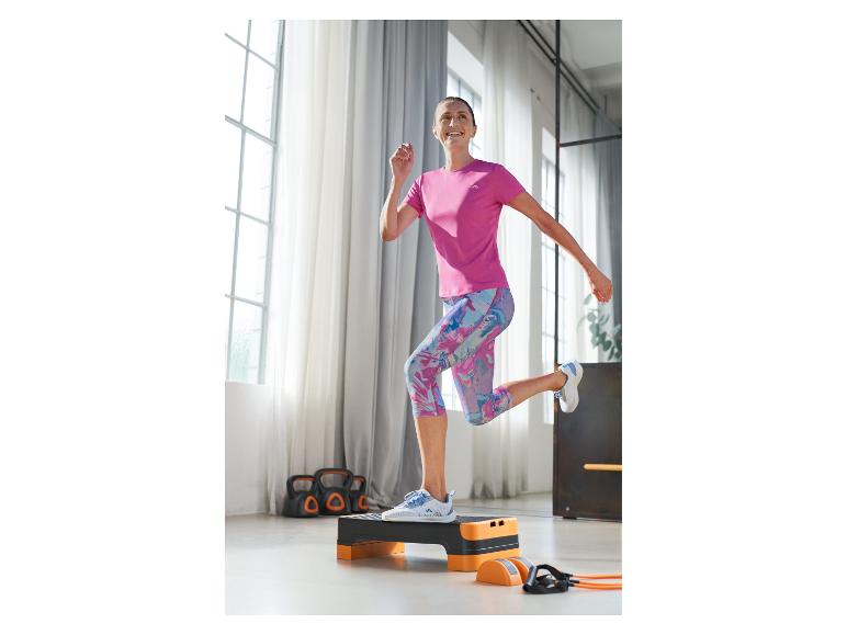 Frau in pinkem Sportshirt und schwarz-orangefarbener Stepbank beim Training