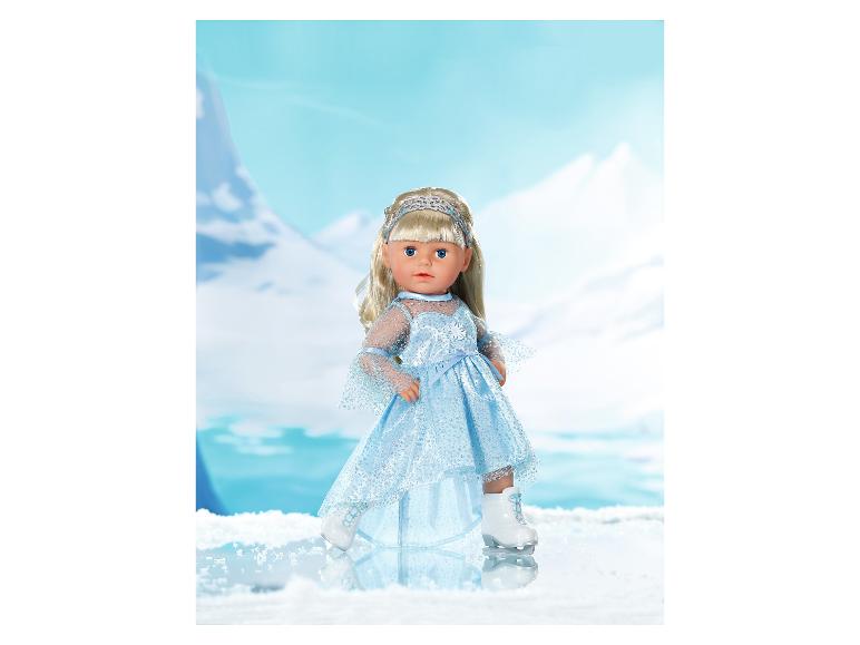Puppe in blauem Kleid und Schlittschuhen, vor bergiger Winterkulisse.