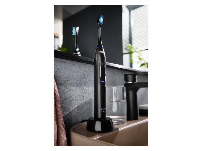 Schwarze elektrische Zahnbürste in Ladestation neben einem Badezimmerwaschbecken.