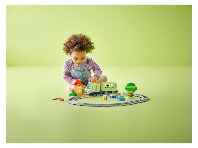 Ein Kind spielt mit einem Spielzeugzug und Bausteinen auf einem grünen Boden.
