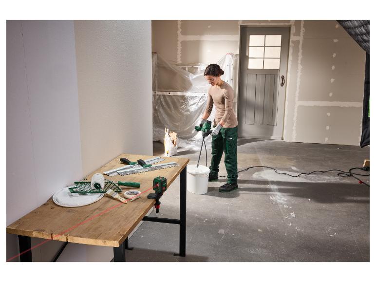 Frau mischt Putz mit einem Rührgerät, Werkzeuge und Laserwasserwaage auf einem Tisch in einem Raum in Renovierung.