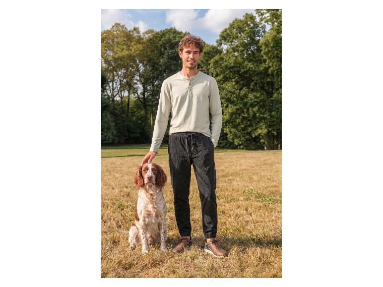 Mann in Langarmshirt und Hose streichelt einen Hund im Freien.