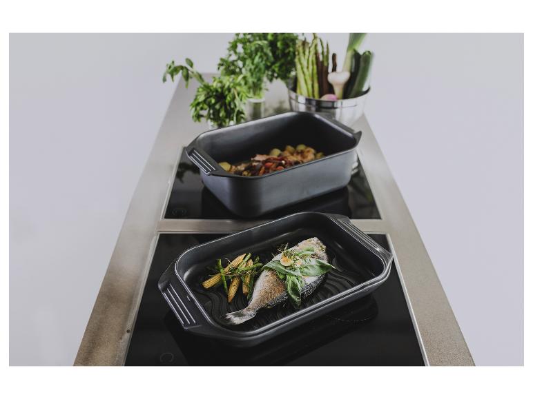 Zwei schwarze Bräter mit gekochtem Fisch und Gemüse auf einem Induktionskochfeld