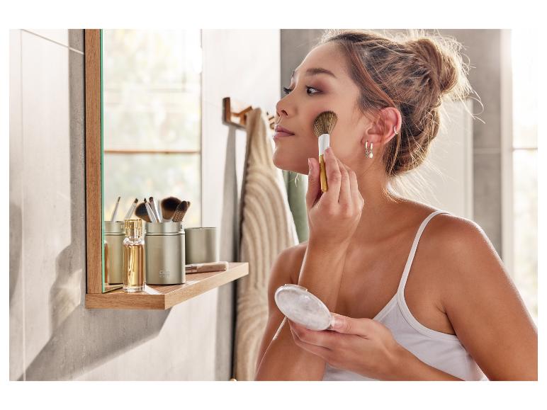 Eine Frau schminkt sich mit einem Pinsel und einem Puderquaste im Badezimmer.