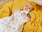 Ein Baby in einem Schlafsack mit Obst-Motiv, das auf einer gelben Decke liegt.