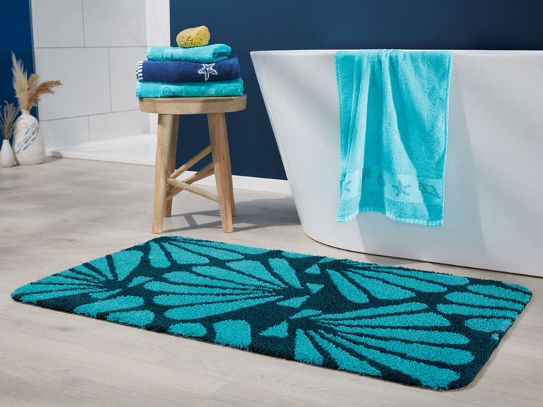 Badematte mit Muschel-Motiv, Handtuch und Handtücher auf einem Holzhocker.