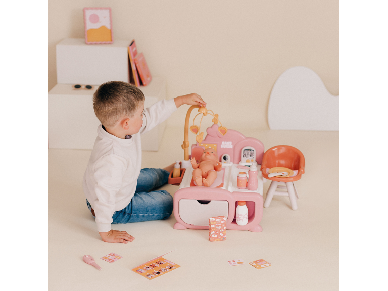 Junge spielt mit einer rosa Puppenpflegestation mit Babypuppe und Zubehör.