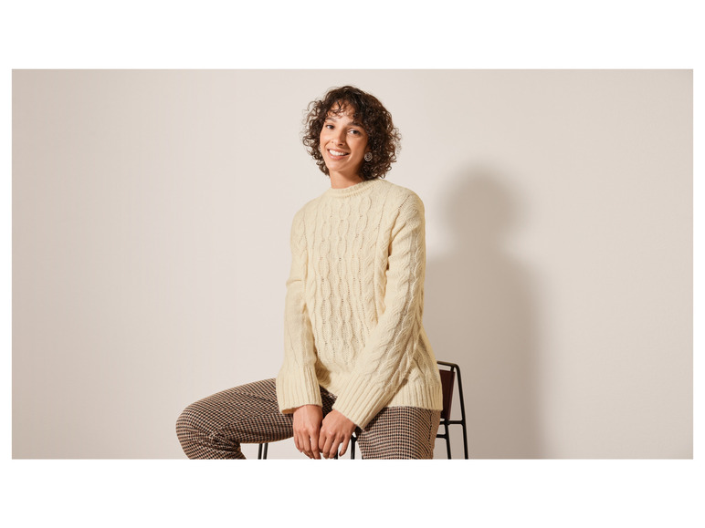 Eine Frau trägt einen cremefarbenen Strickpullover und eine Hose mit Karomuster.