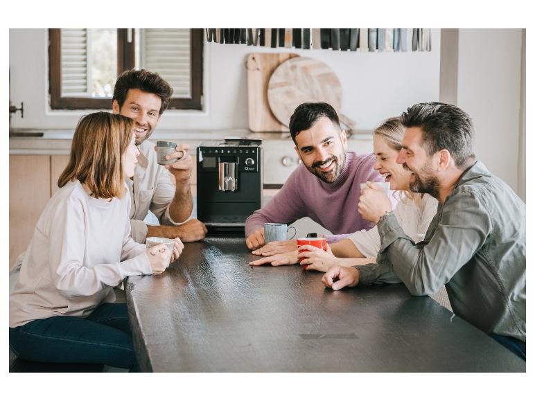 Freunde genießen Kaffee und Unterhaltung an einem Tisch mit einer Kaffeemaschine.