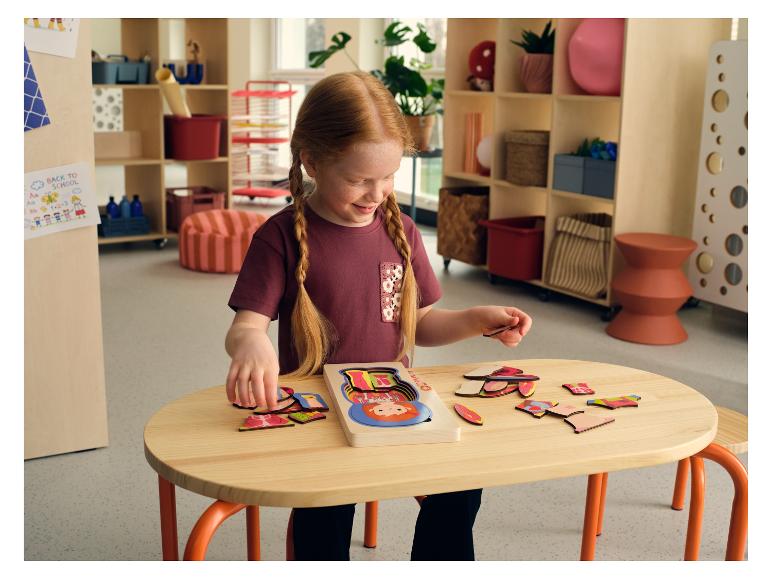 Ein junges Mädchen spielt an einem Tisch mit einem LUPILU® Körper-Puzzle aus Holz.