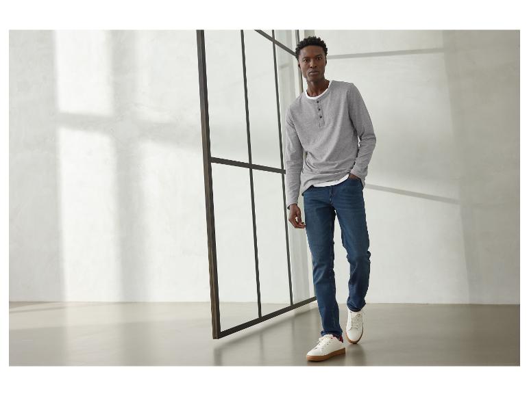 Mann in grauem Langarmshirt, blauen Jeans und weißen Sneakern.