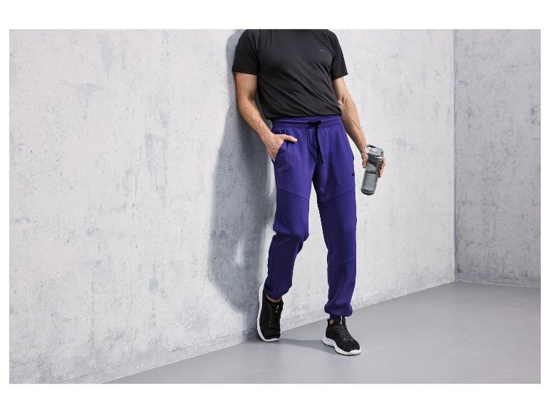 Mann in schwarzem T-Shirt und blauen Jogginghose mit Wasserflasche.