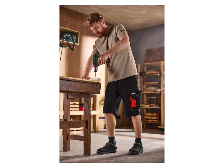 Mann in Arbeitsshorts und T-Shirt benutzt einen Akkuschrauber an einer Holzwerkbank.