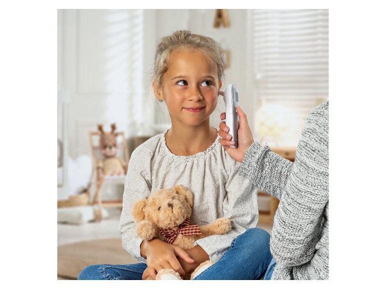 Mädchen mit Teddybär, ihre Temperatur wird mit einem Ohrthermometer gemessen.