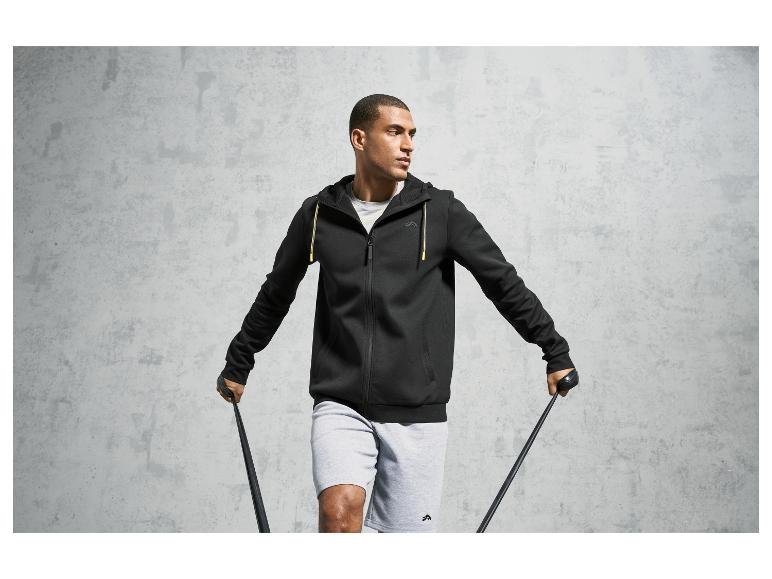 Mann in schwarzem Hoodie und grauen Shorts mit Fitnessgummi.