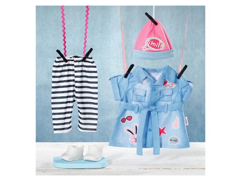 Puppenkleidung: gestreifte Hose, blaues Gürtelkleid und rosa „Smile“-Mütze trocknen an der Leine.