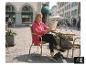 Frau in rosa Hemd und schwarzer Hose liest Zeitung an einem Straßencafé-Tisch.