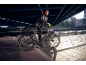 Mann in Sportkleidung mit Fahrrad unter einer Brücke, städtische Umgebung.