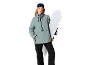 Frau in grüner Skijacke und schwarzer Skihose mit Snowboard und Skibrille.