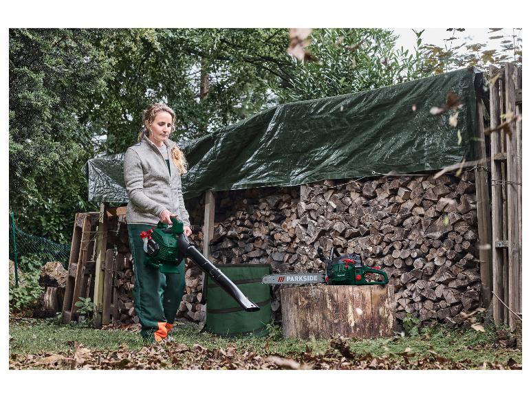 Frau benutzt Laubbläser, mit Kettensäge auf einem Holzstamm.