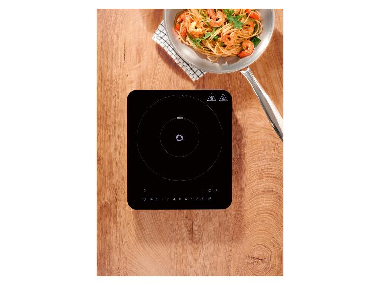 Induktionskochfeld mit einer Pfanne Garnelenpasta auf einer Holzoberfläche.