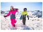 Zwei Kinder in Skianzügen, Helmen und Skibrillen gehen im Schnee mit Skiern und Stöcken.