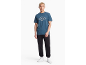 Mann in blauem T-Shirt mit Rautenmuster, schwarzer Jogginghose und weißen Turnschuhen.