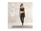 Eine Frau in schwarzen Leggings und Sport-BH steht auf einer Yogamatte.