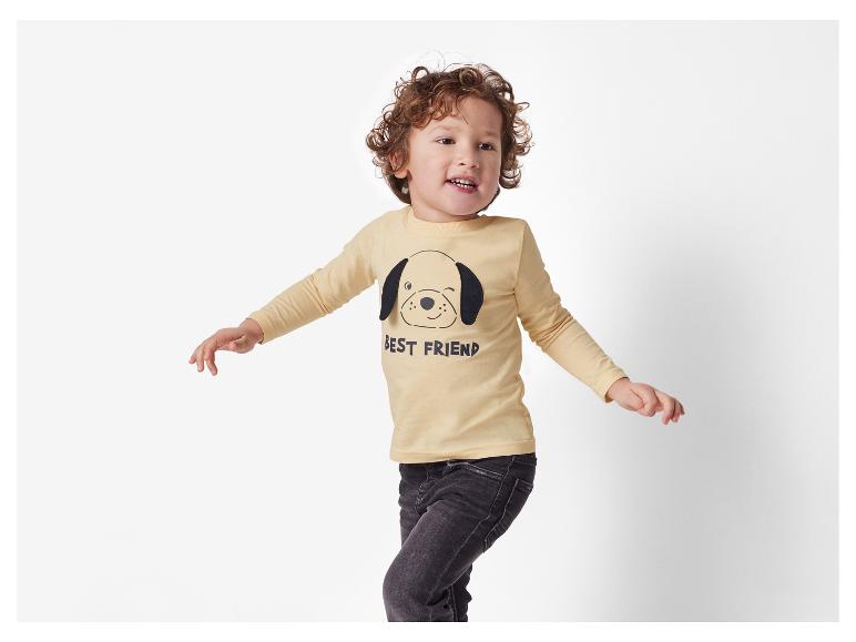 Ein kleiner Junge trägt ein gelbes T-Shirt mit einem Hundeaufdruck und dem Text 'Bester Freund'.