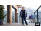 Junge in Winterjacke, Jeans und Stiefeln auf einer verschneiten Terrasse.