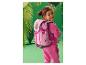 Lächelndes Mädchen im pinken Trainingsanzug mit pinkem Rucksack mit Cartoon-Hund und Dinosaurier-Prints.