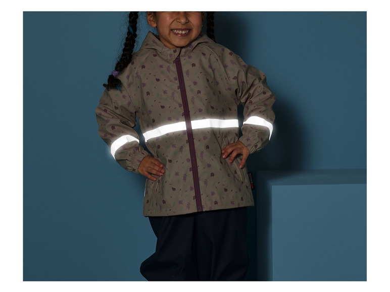 Ein Kind trägt eine Regenjacke mit reflektierenden Streifen und eine Hose.