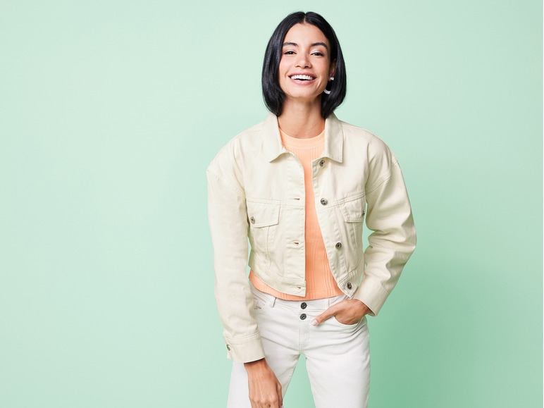 Eine Frau trägt eine weiße Jeansjacke, ein rosafarbenes T-Shirt und weiße Jeans.