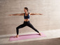 Eine Frau macht Yoga in Sportkleidung auf einer rosa Matte.