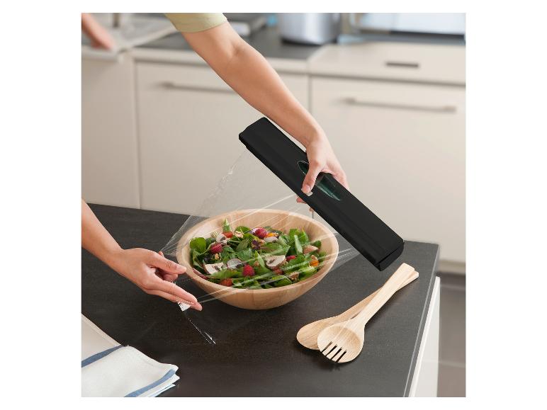 Eine Frau benutzt einen schwarzen Frischhaltefolienspender in der Küche, um einen Salat abzudecken.