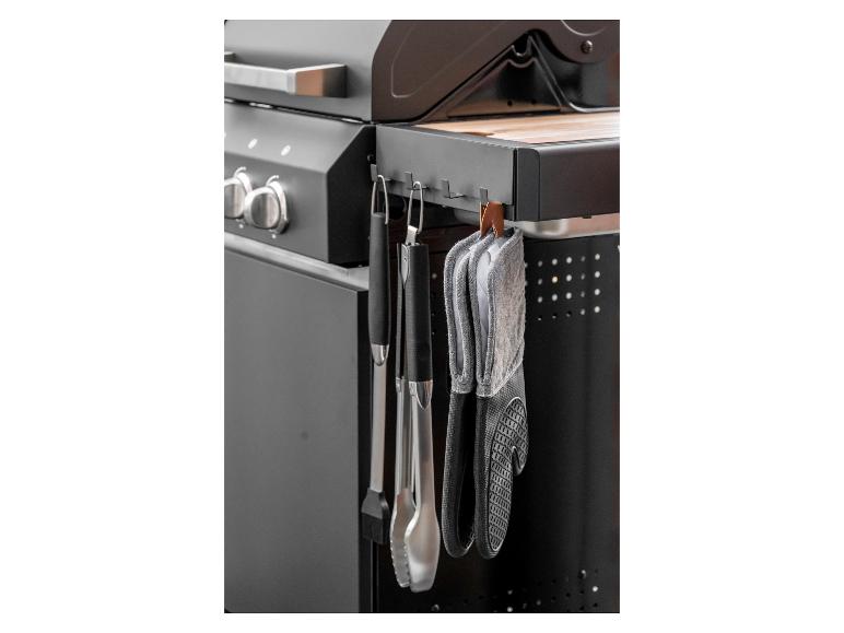 Grillhandschuhe und Grillzubehör hängen an einem schwarzen Grill.