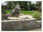 Steingartenbrunnen mit Blocksteinmauer und Blumen.