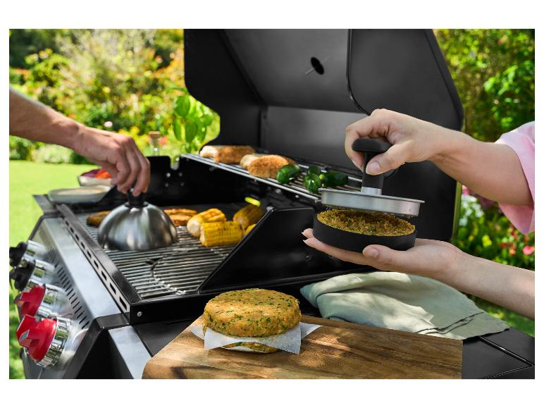 Zwei Hände bereiten Burger und Mais auf einem Außengrill zu.
