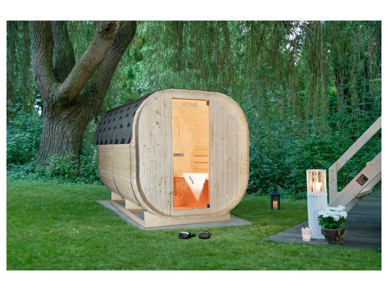 HOME DELUXE Holzfasssauna in einem grünen Garten mit Bäumen.