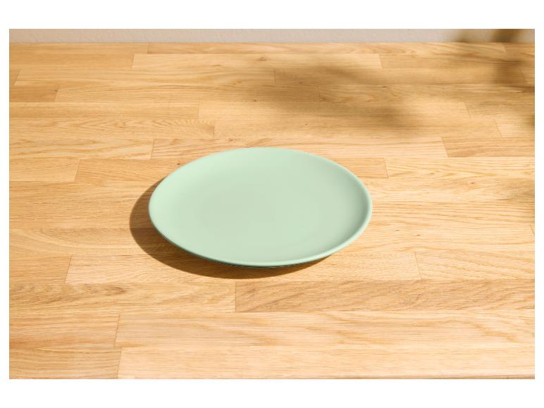 Hellgrüner Teller auf einem hellen Holztisch mit Schatten